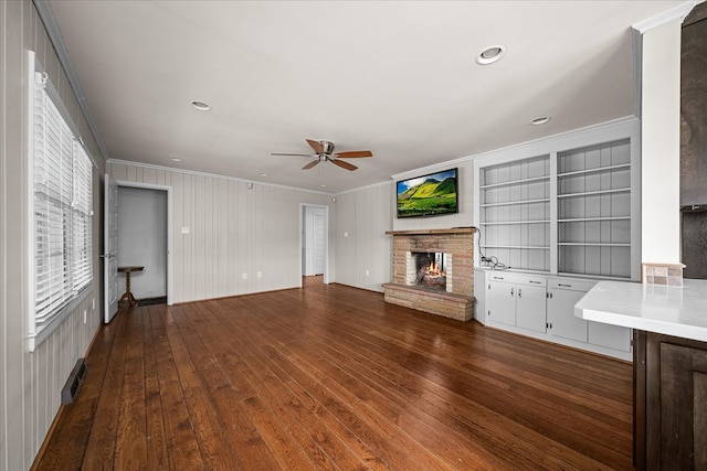 unfurnished living room featuring dark wood-style floors, a fireplace, a ceiling fan, and crown molding