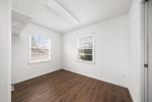 empty room with baseboards, visible vents, and dark wood finished floors