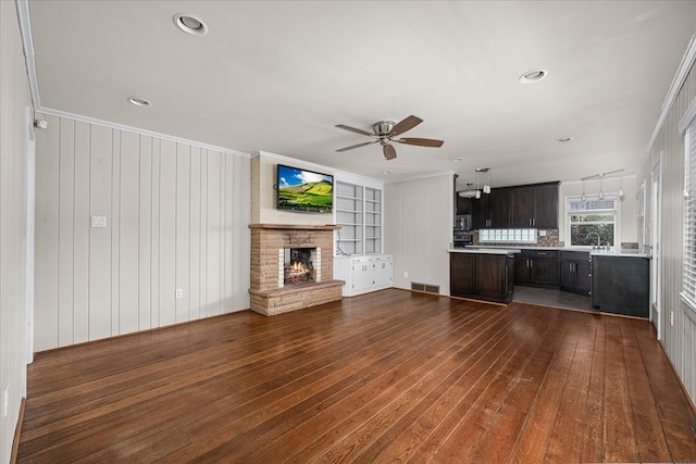 unfurnished living room featuring visible vents, dark wood finished floors, a ceiling fan, built in features, and a lit fireplace