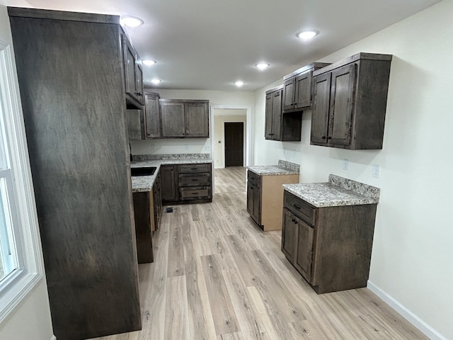 kitchen with dark brown cabinetry, light wood-style flooring, light countertops, and baseboards