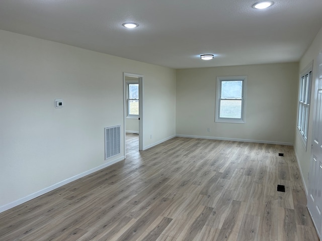 spare room featuring a wealth of natural light, visible vents, light wood-style flooring, and baseboards