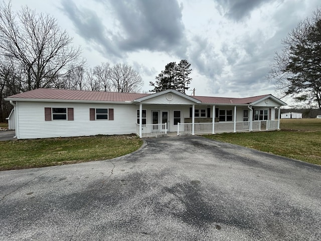 single story home featuring aphalt driveway, a porch, metal roof, and a front yard