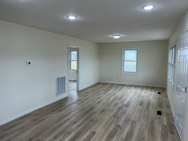 empty room featuring a wealth of natural light, visible vents, baseboards, and wood finished floors