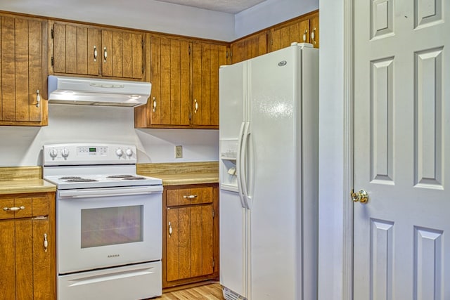 kitchen featuring brown cabinets, light countertops, light wood-style flooring, white appliances, and under cabinet range hood