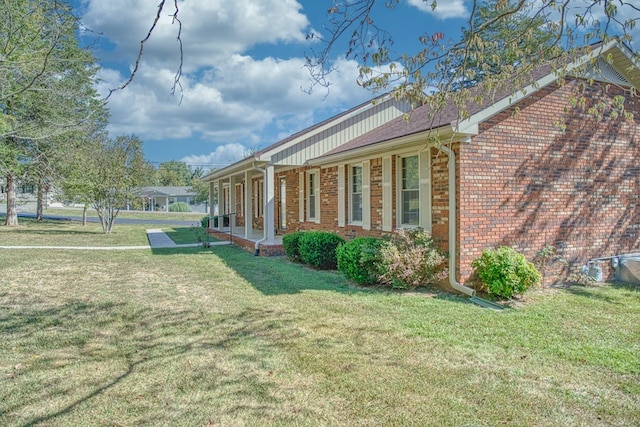 view of side of property featuring covered porch, brick siding, and a lawn