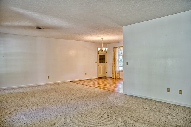 unfurnished room featuring a chandelier, a textured ceiling, and baseboards