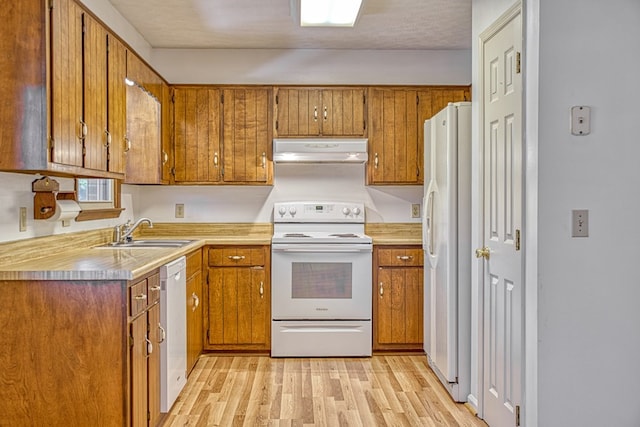 kitchen with white appliances, under cabinet range hood, brown cabinets, and a sink