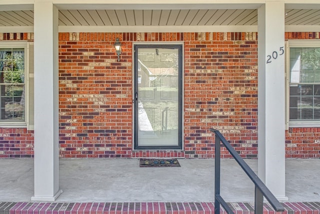 view of exterior entry featuring a porch and brick siding