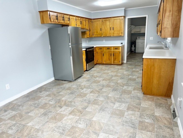 kitchen with light countertops, electric range, freestanding refrigerator, a sink, and washer / dryer