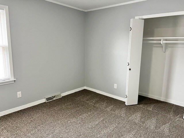 unfurnished bedroom featuring ornamental molding, dark carpet, visible vents, and baseboards