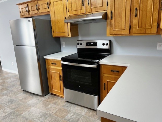 kitchen with under cabinet range hood, baseboards, light countertops, appliances with stainless steel finishes, and brown cabinetry