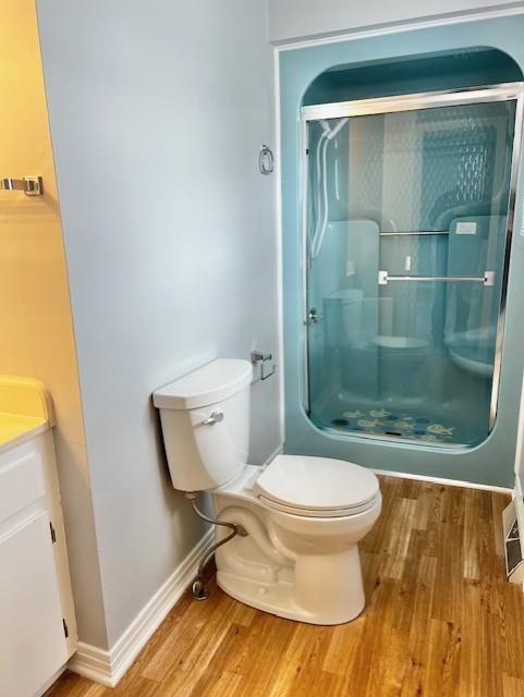 bathroom with toilet, a stall shower, wood finished floors, and vanity