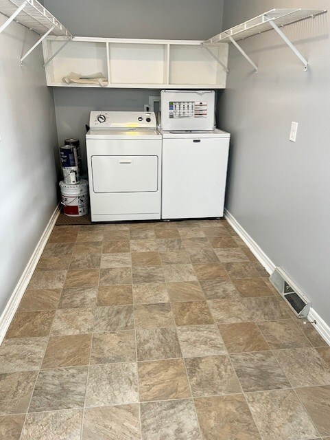 washroom featuring laundry area, washer and clothes dryer, visible vents, baseboards, and stone finish floor