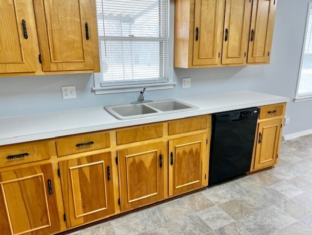 kitchen with black dishwasher, light countertops, brown cabinetry, a sink, and baseboards