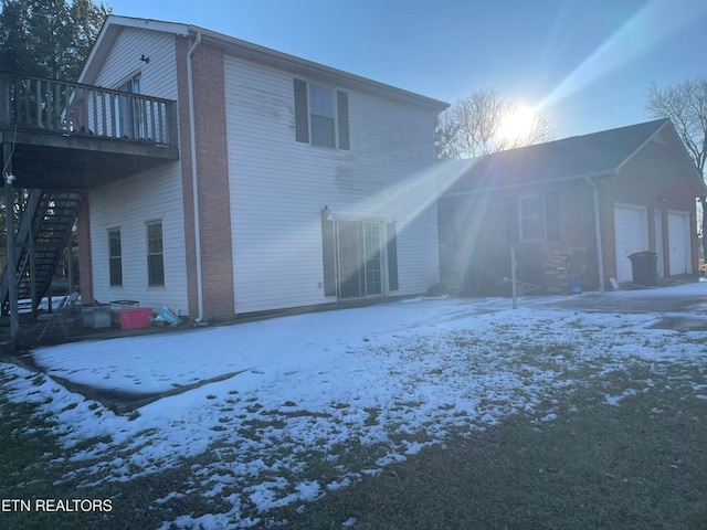 snow covered rear of property featuring a garage and stairs