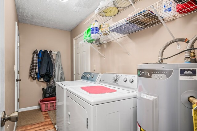 clothes washing area with laundry area, electric water heater, a textured ceiling, light wood-type flooring, and separate washer and dryer