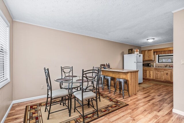 dining area featuring baseboards, a dry bar, a textured ceiling, and light wood finished floors