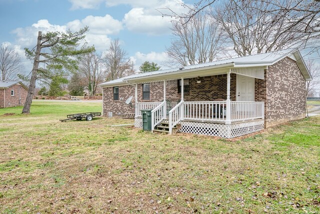 ranch-style home featuring a porch, a front yard, brick siding, and metal roof