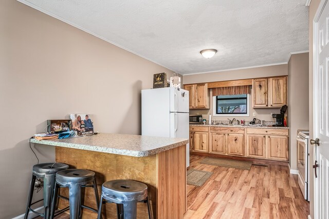 kitchen with light wood-style flooring, a peninsula, white appliances, light countertops, and a kitchen bar