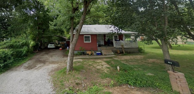 bungalow-style home with a carport, a front yard, covered porch, and gravel driveway