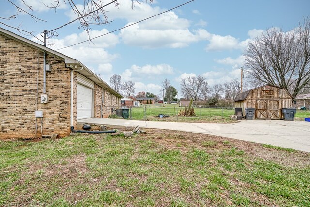 view of yard featuring a garage, an outbuilding, concrete driveway, and fence