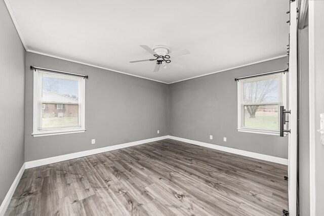 spare room with ornamental molding, a healthy amount of sunlight, baseboards, and wood finished floors