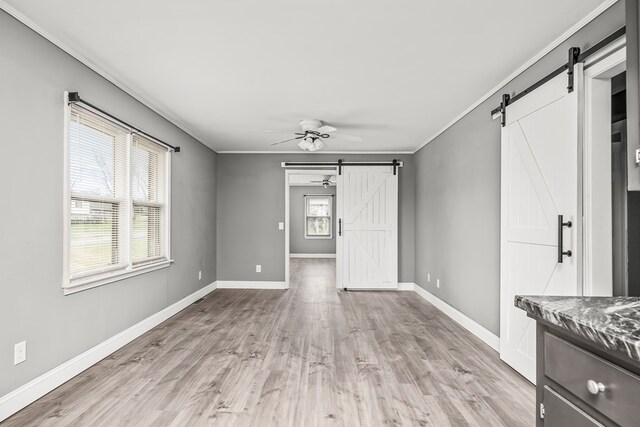 interior space featuring a barn door, baseboards, ceiling fan, ornamental molding, and light wood-type flooring