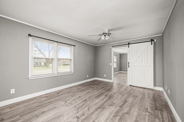 unfurnished bedroom featuring light wood-type flooring, crown molding, baseboards, and a barn door