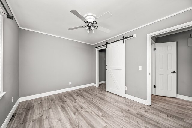 unfurnished bedroom featuring a barn door, visible vents, baseboards, ornamental molding, and light wood-type flooring