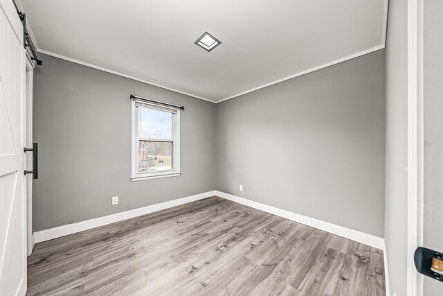 empty room with baseboards, a barn door, light wood-style flooring, and crown molding