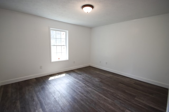 spare room featuring dark wood-style flooring, a textured ceiling, and baseboards