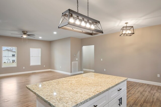 kitchen featuring pendant lighting, white cabinets, open floor plan, and light stone countertops