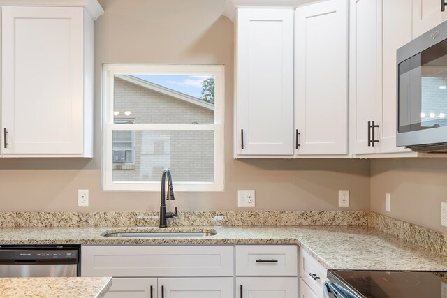 kitchen featuring stainless steel appliances, white cabinets, a sink, and light stone countertops