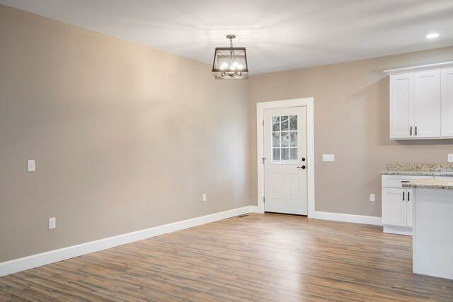 unfurnished dining area featuring a notable chandelier, wood finished floors, and baseboards