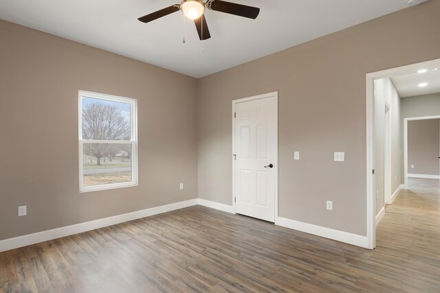 spare room with dark wood finished floors, a ceiling fan, and baseboards