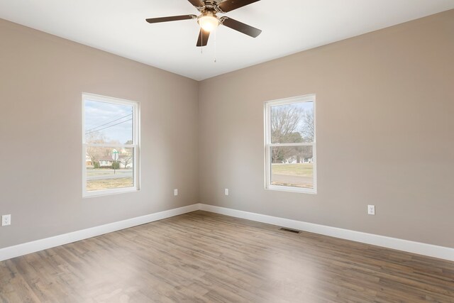 empty room featuring a ceiling fan, wood finished floors, visible vents, and baseboards