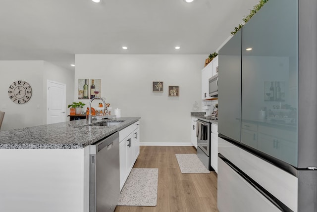 kitchen with light wood-style flooring, stainless steel appliances, a sink, white cabinets, and dark stone counters