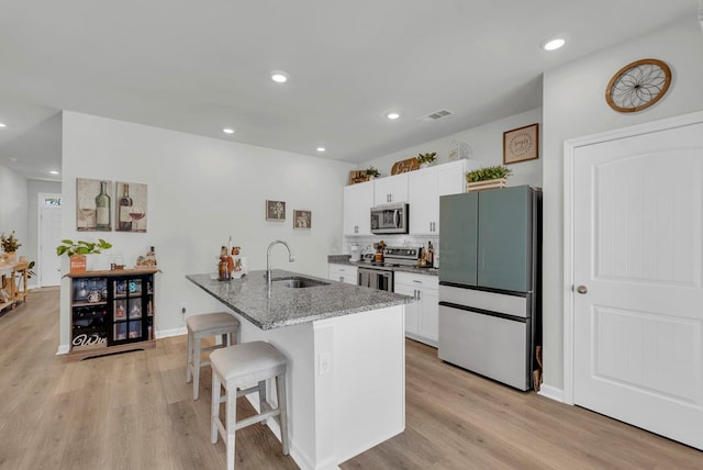 kitchen with visible vents, a breakfast bar, dark stone countertops, stainless steel appliances, and a sink