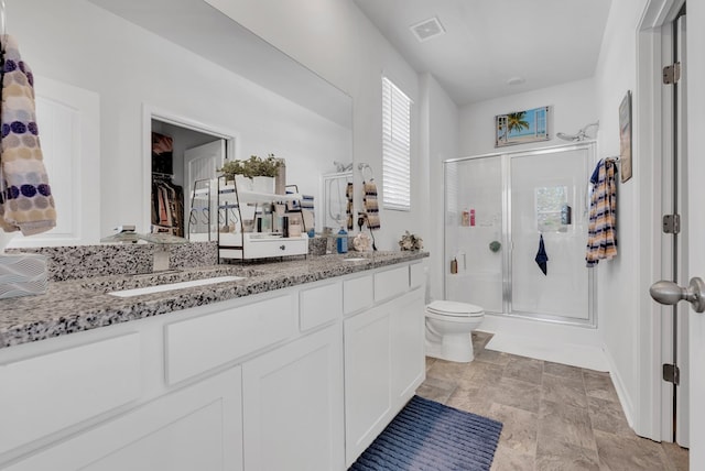 bathroom featuring double vanity, visible vents, toilet, a stall shower, and a sink