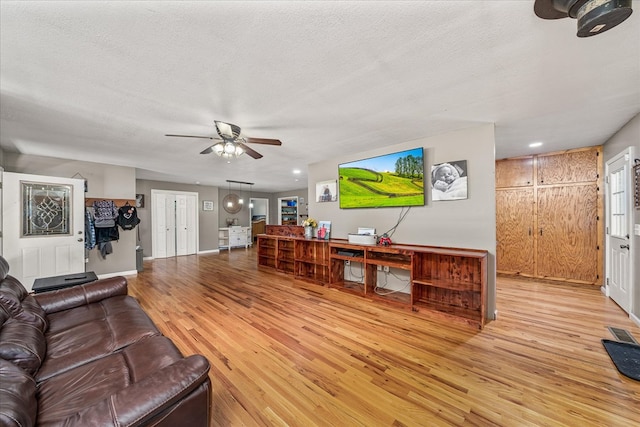 living area with a textured ceiling, light wood finished floors, visible vents, and a ceiling fan