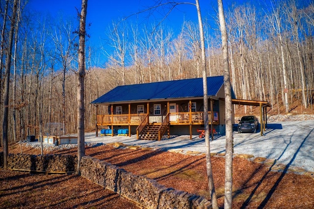 view of front of home featuring metal roof, covered porch, a carport, gravel driveway, and a wooded view