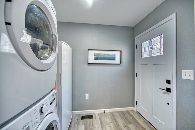 laundry room featuring stacked washer and dryer, a textured wall, light wood-style floors, and baseboards