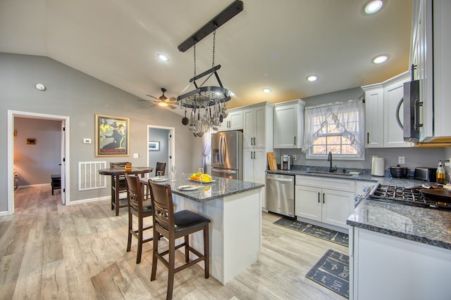 kitchen with stainless steel appliances, a sink, visible vents, white cabinets, and a center island