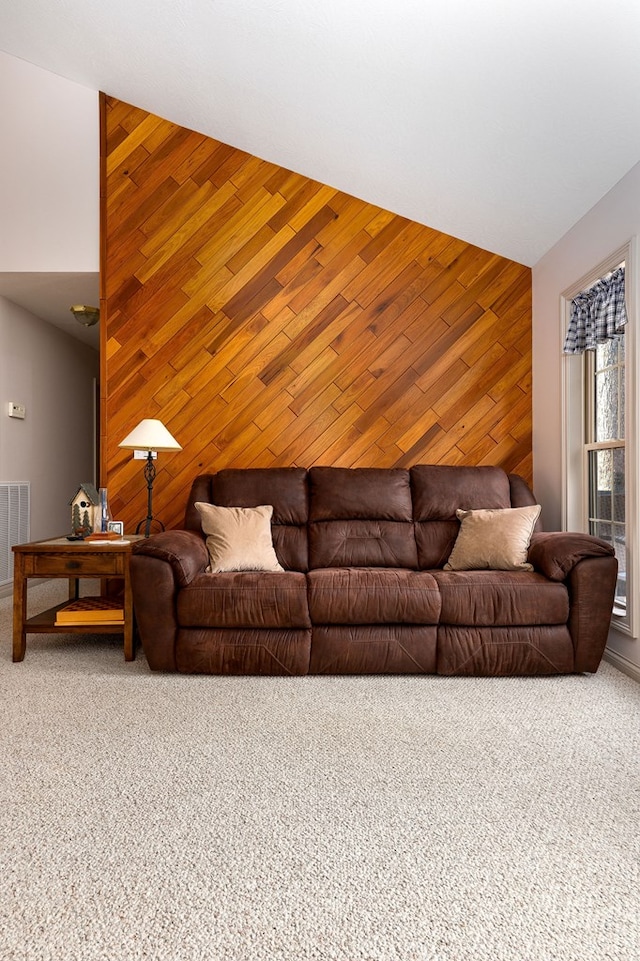 living room with visible vents, an accent wall, vaulted ceiling, carpet floors, and wood walls