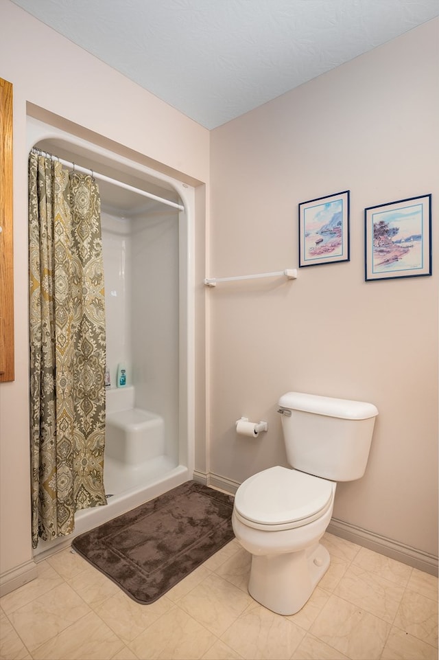 bathroom with toilet, a stall shower, and baseboards