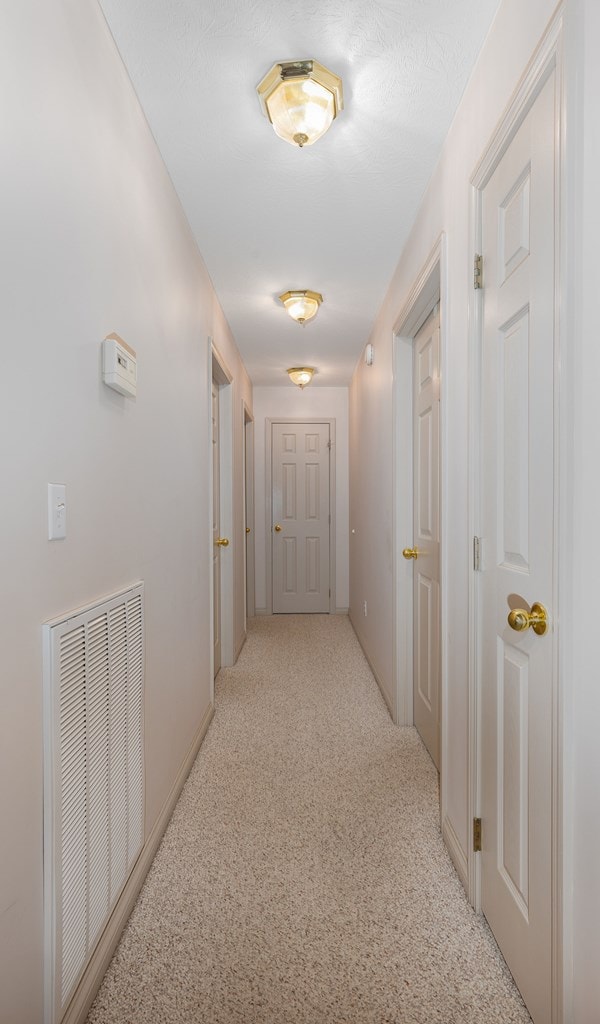 hallway featuring visible vents and light colored carpet