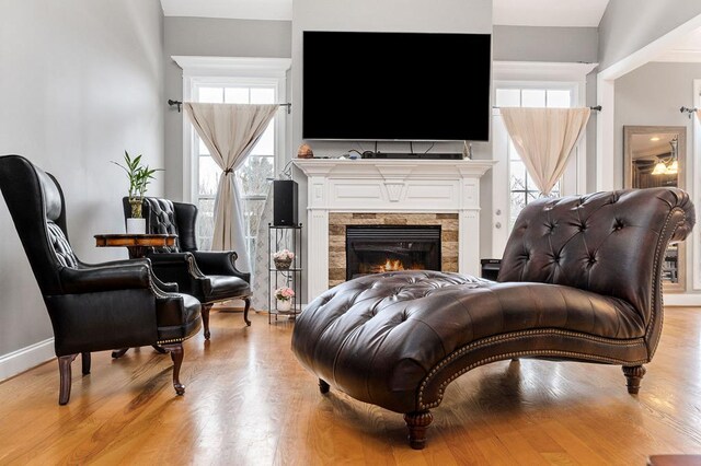 sitting room featuring a lit fireplace, baseboards, and light wood-style flooring