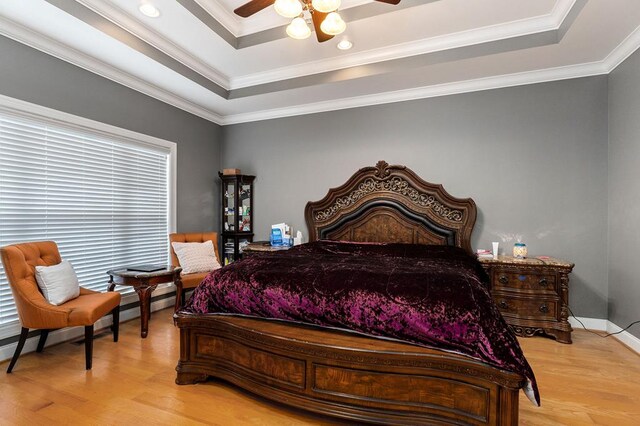 bedroom with light wood-style floors, a tray ceiling, and ornamental molding