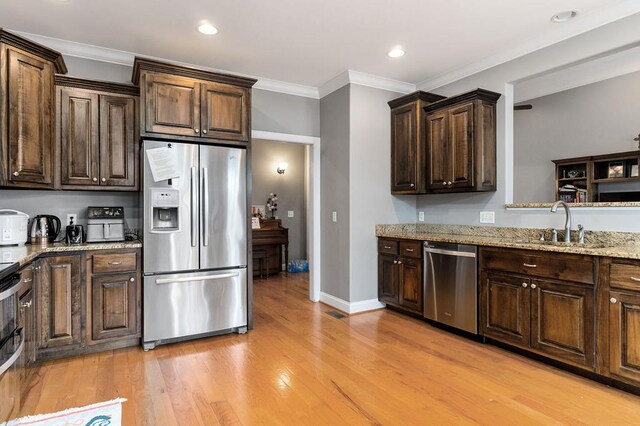 kitchen featuring light wood finished floors, light stone counters, stainless steel appliances, crown molding, and a sink