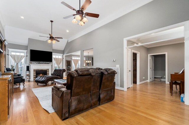 living room with lofted ceiling, a stone fireplace, light wood-type flooring, baseboards, and ceiling fan with notable chandelier